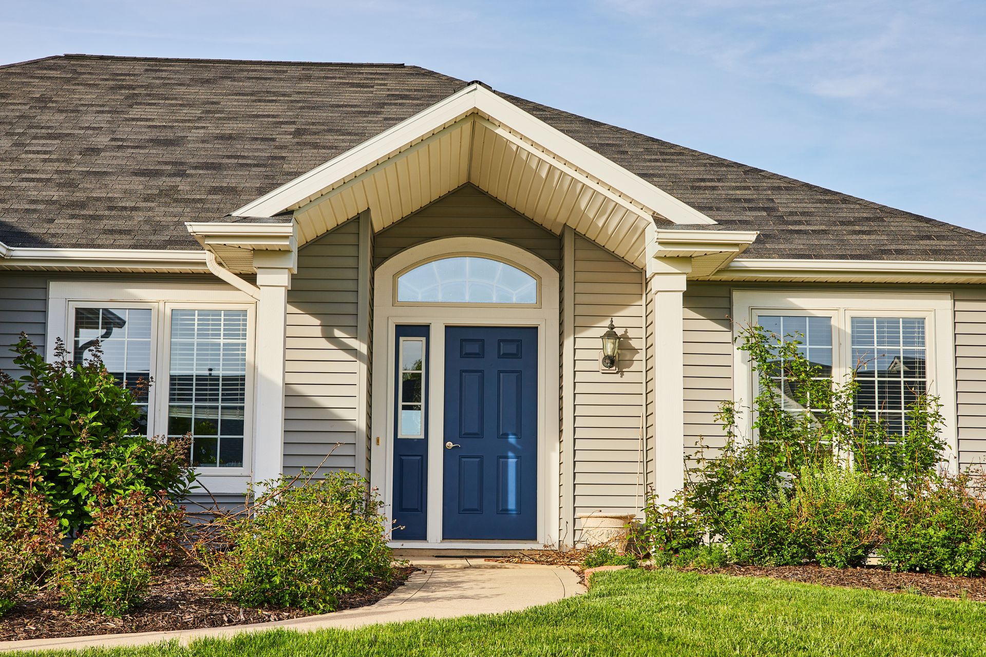 Blue front door of a gray-sided house with white trim, set in a green yard with a path.