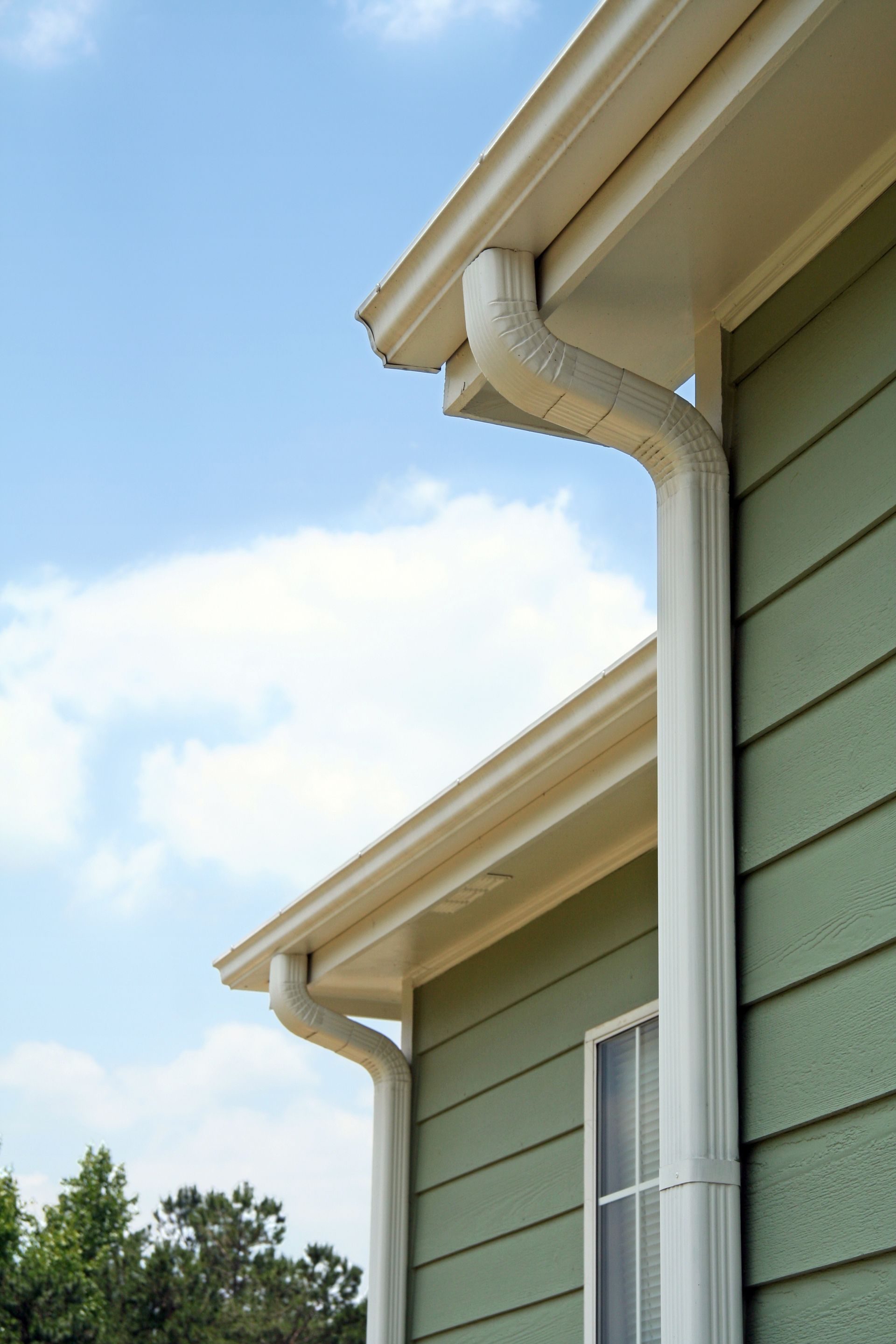 White gutters on green siding of a house, with blue sky and clouds in the background. White gutters on green siding of a house, with blue sky and clouds in the background.