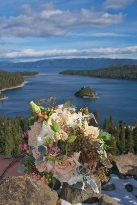 Bouquet with white, pink, and peach flowers overlooking a lake and mountains under a blue sky.