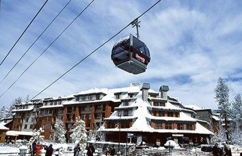 Cable car above snow-covered building in a ski resort under a partly cloudy sky.