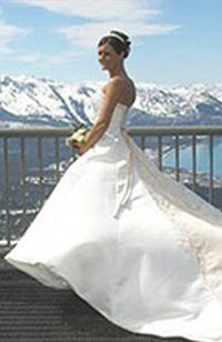 Bride in white strapless gown holds bouquet, poses with mountain backdrop.
