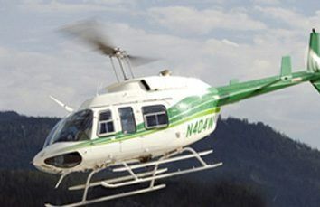 White and green helicopter in flight over a forested mountain landscape; registration number N404AW.