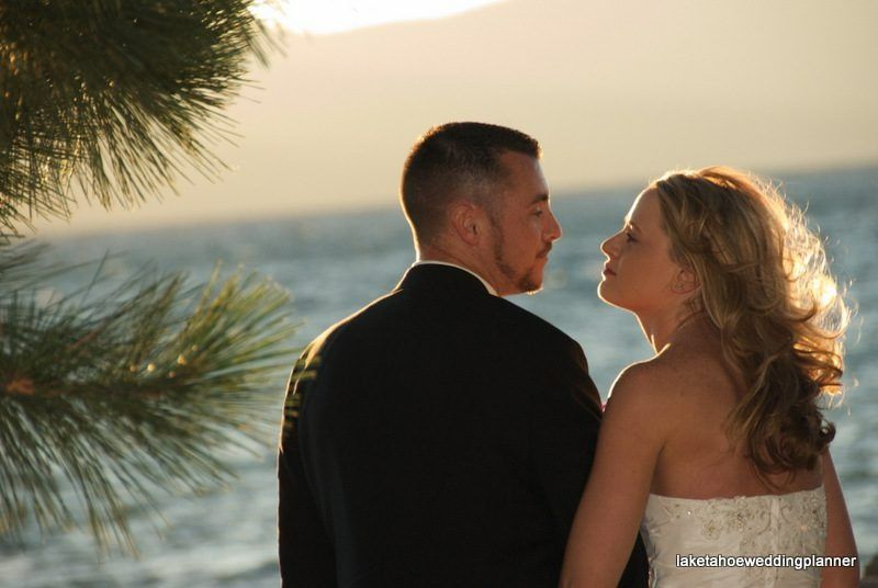 Couple facing each other by the water at sunset. The woman wears a white dress; the man, a black suit.