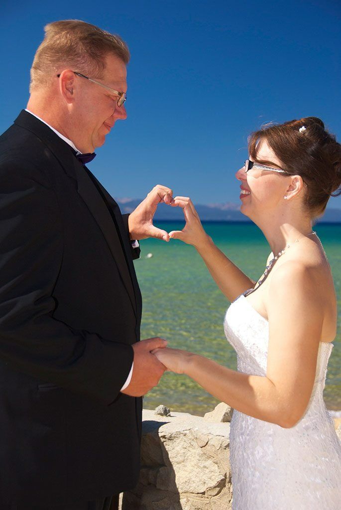 Couple at wedding, making heart shape with hands, ocean and blue sky background.