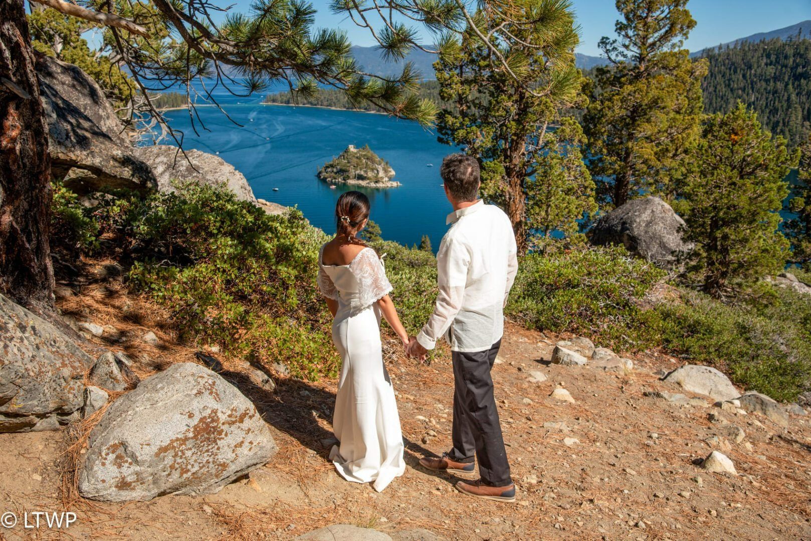 Couple in wedding attire overlooking lake and island.
