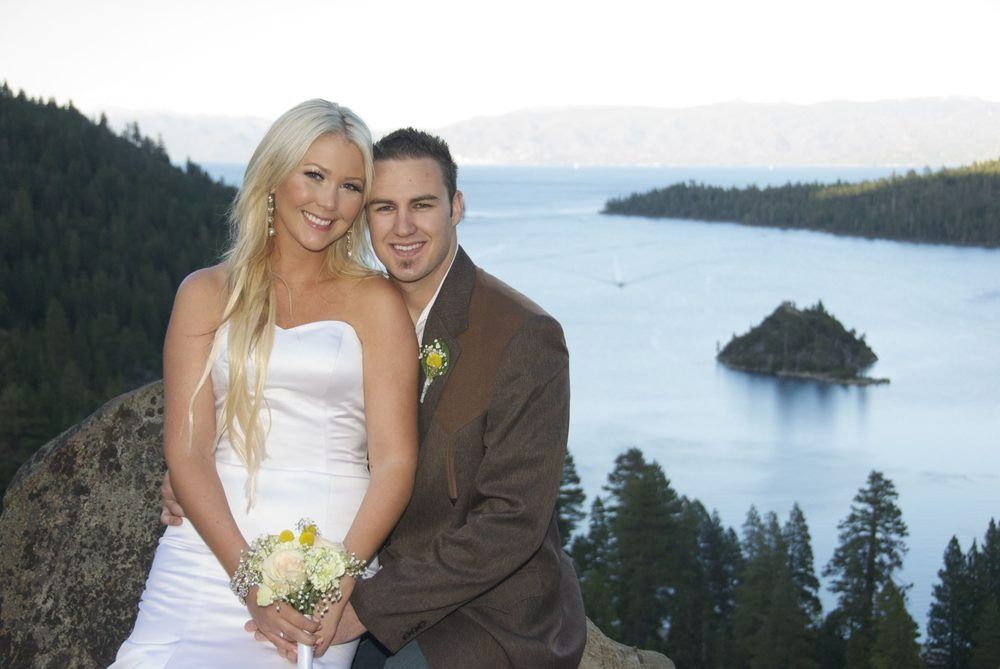 Bride and groom smiling at camera, lake and island in background.