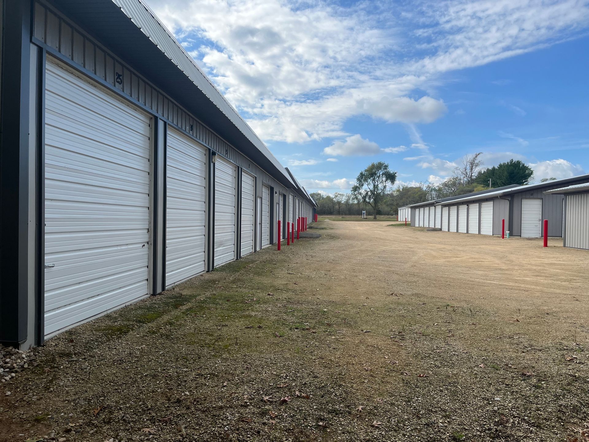 Row of storage units with white doors, grassy area, blue sky with clouds.