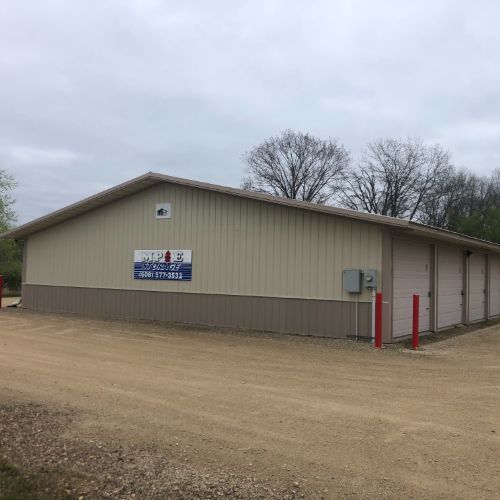 Tan storage units with a business sign, set on a gravel lot under a cloudy sky.