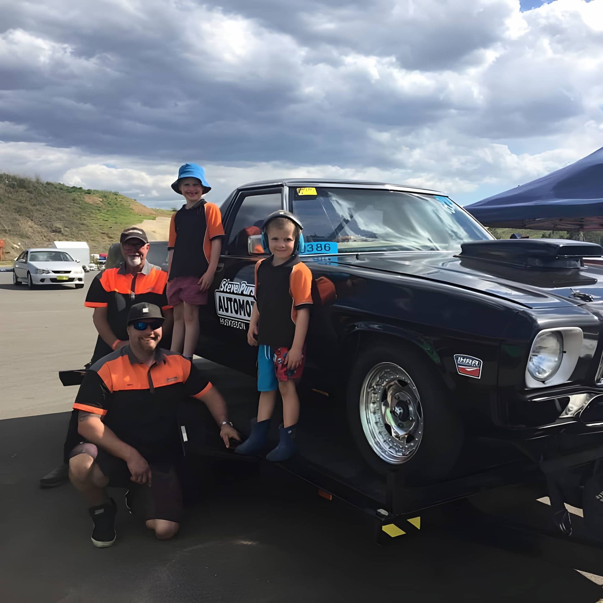 A Group of People Posing in Front of A Black Truck that Says ' Racing ' on The Side — Steve Purse Automotive In Huskisson, NSW