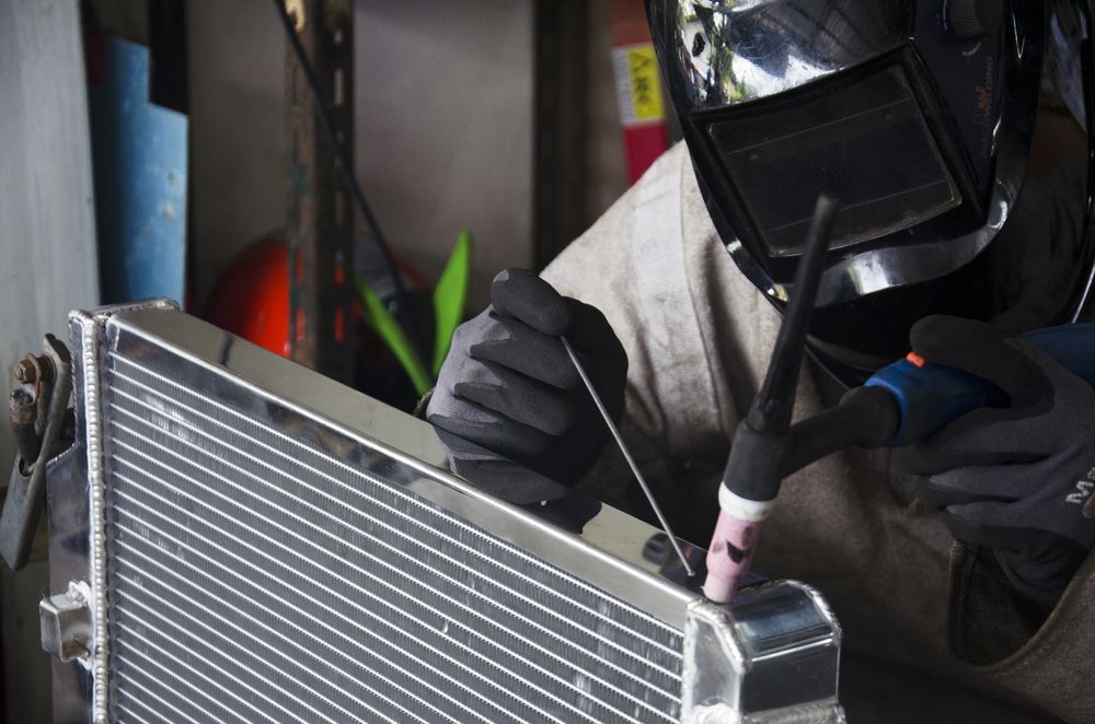 A Man Wearing a Welding Helmet Is Welding a Radiator — Steve Purse Automotive In Falls Creek, NSW