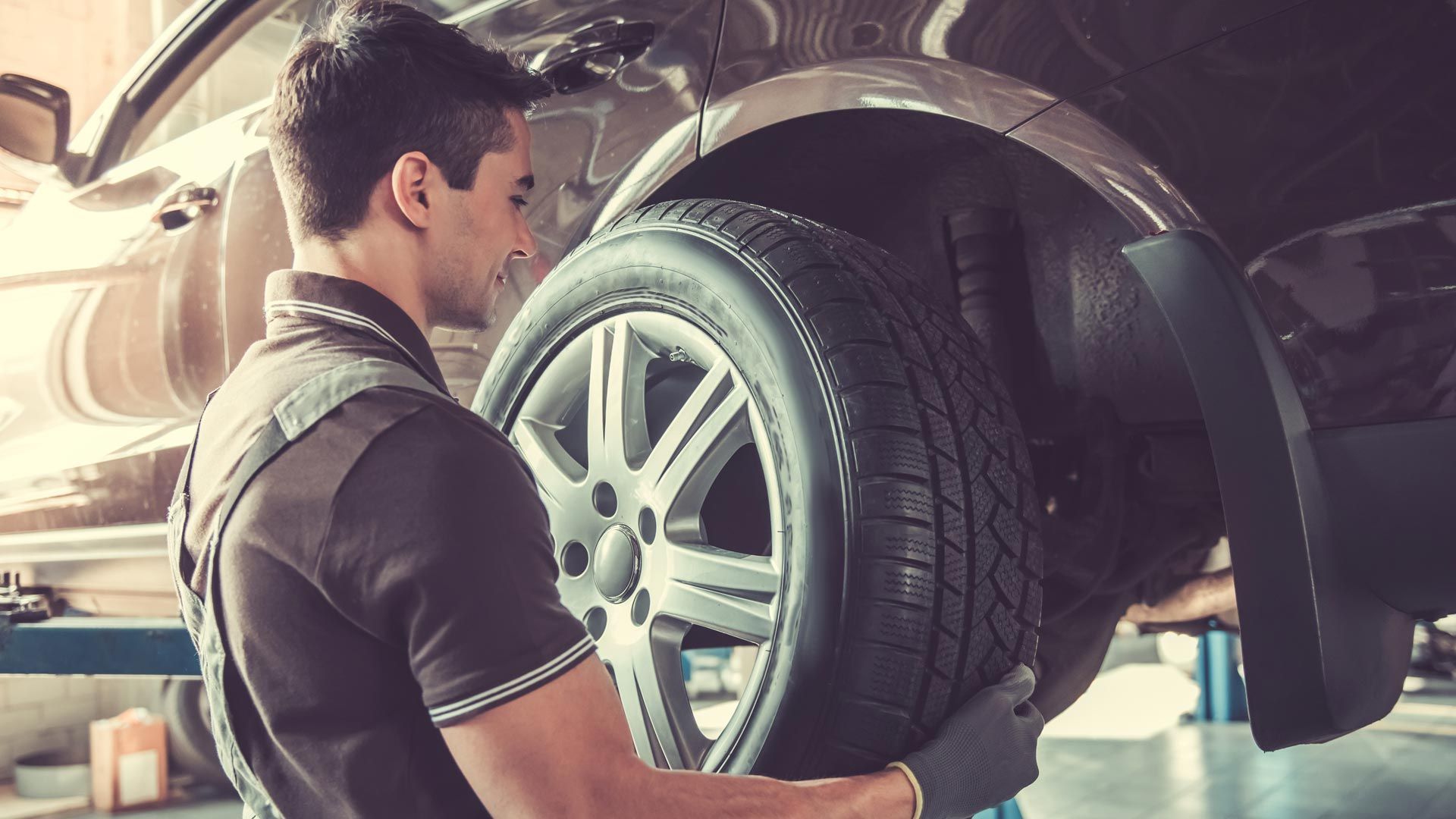 A Man Is Changing a Tire on A Car in A Garage — Steve Purse Automotive In Falls Creek, NSW