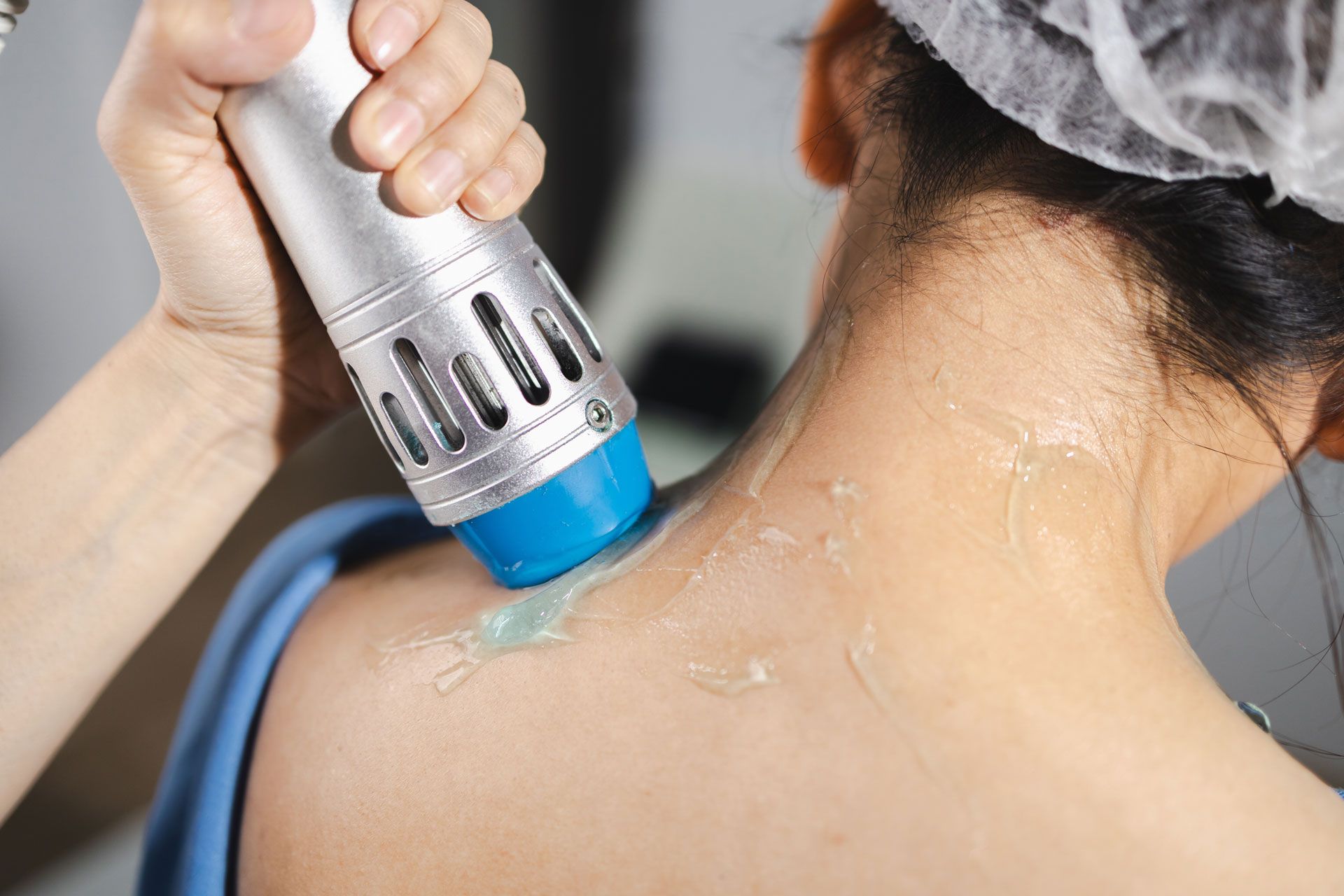 A person receiving shockwave therapy on the neck. A device is held against the skin, with gel visible.