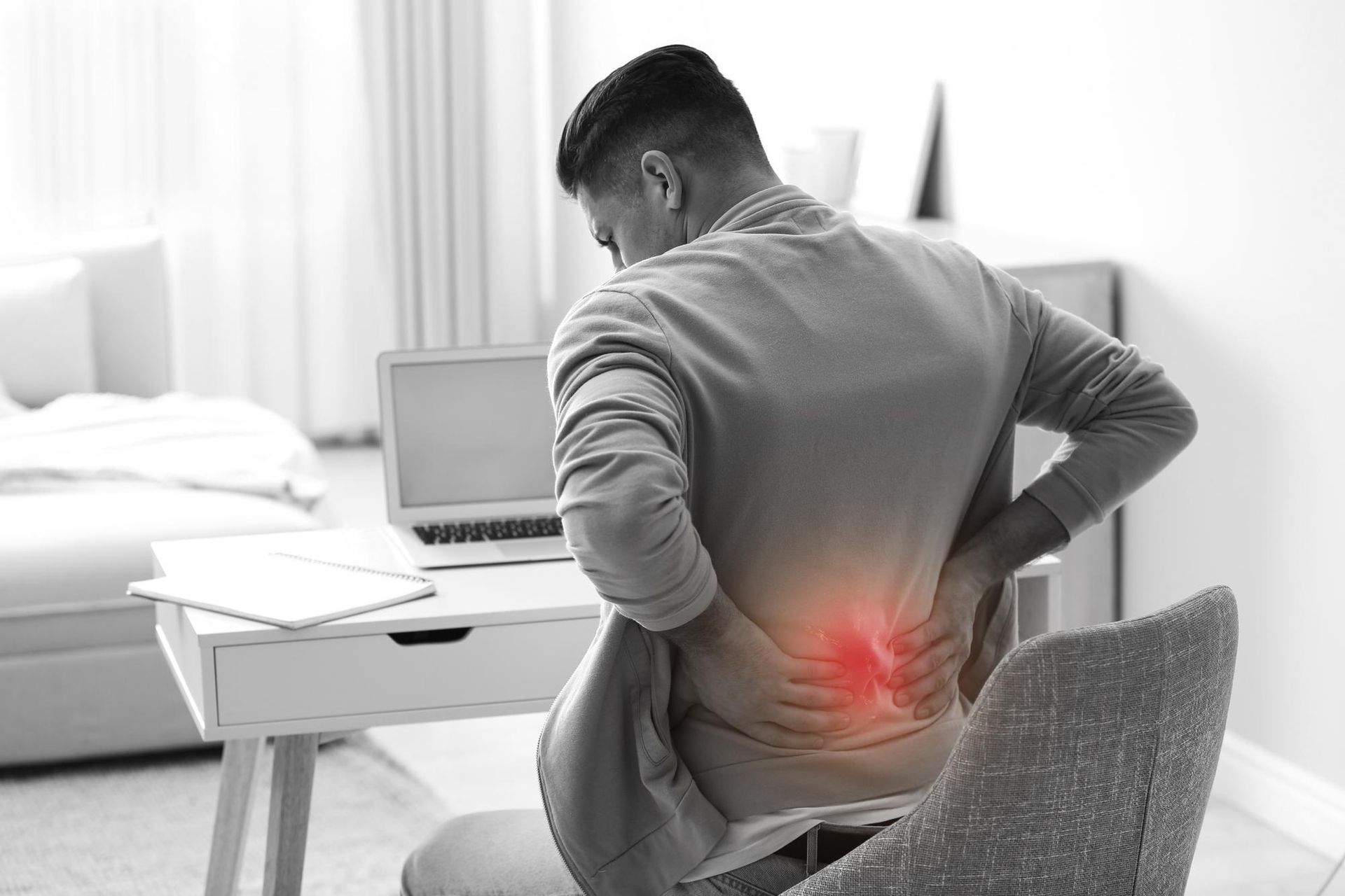 a man is sitting at a desk with his back in pain .