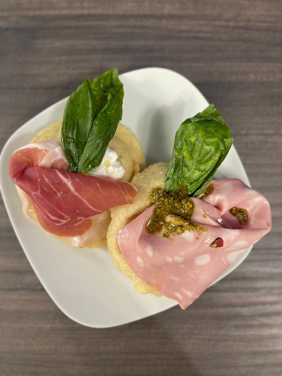 Due gustosi antipasti serviti su un piatto bianco, ciascuno guarnito con salumi piegati, una foglia di basilico e salsa.