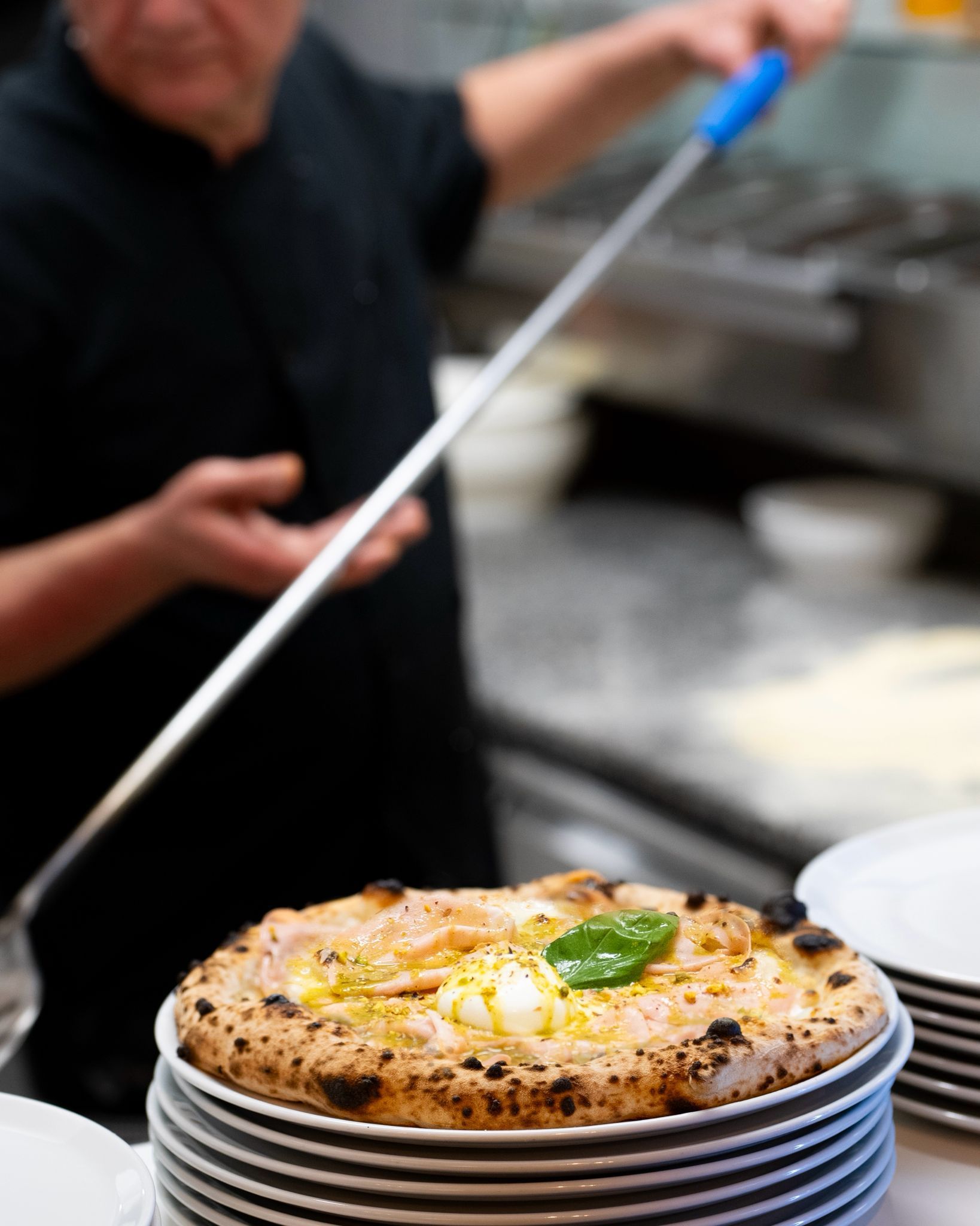 Una pizza cotta nel forno a legna con pomodoro, mozzarella fusa, fette di cipolla rossa e salumi, servita su un piatto.