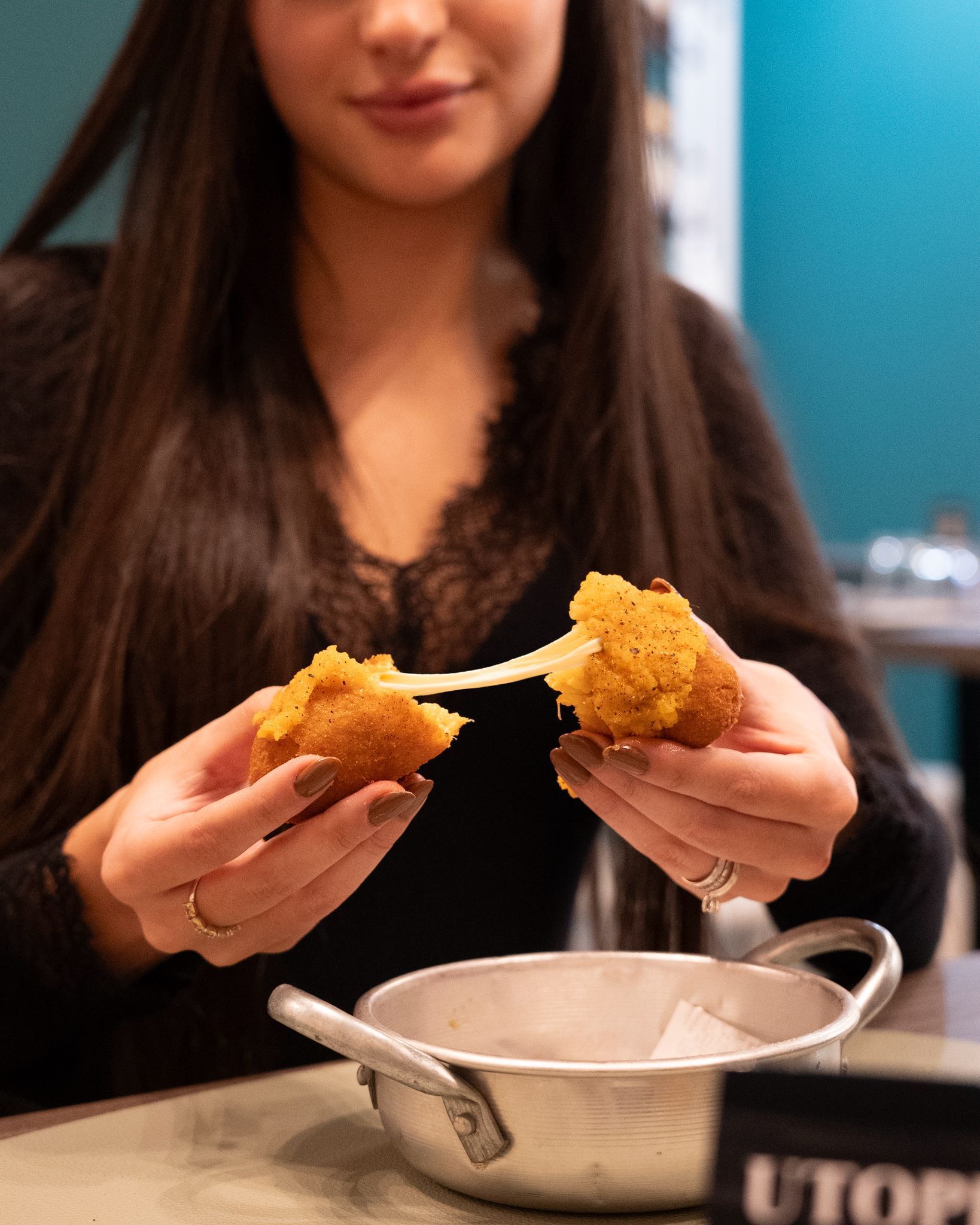 Un bastoncino di formaggio impanato e dorato, spezzato a metà, rivela un formaggio fuso ed elastico che unisce le due parti.