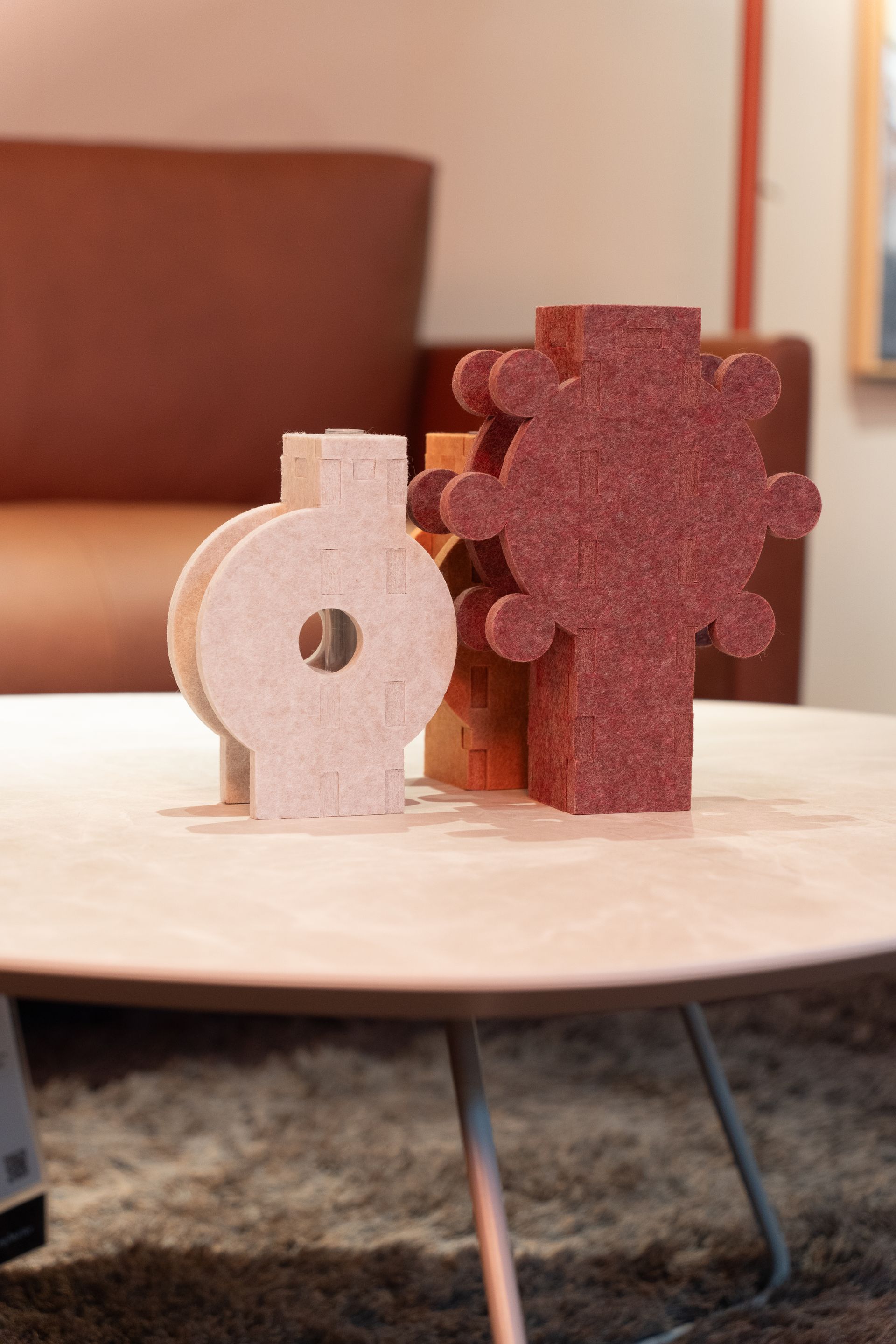 Drie abstracte decoratieve objecten op een lichtbruine tafel. De vormen zijn beige, oranje en roodbruin.