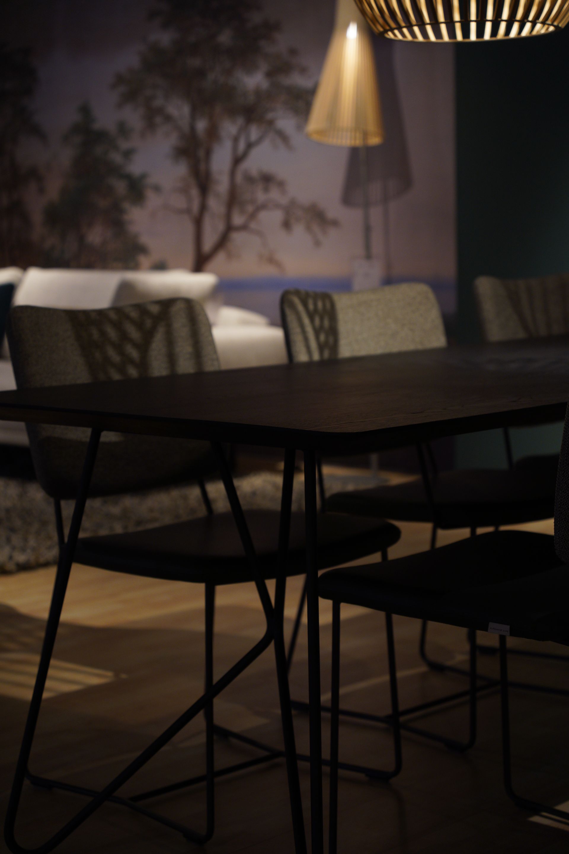 Dining table with chairs in front of a wall mural. Overhead light illuminates the scene.