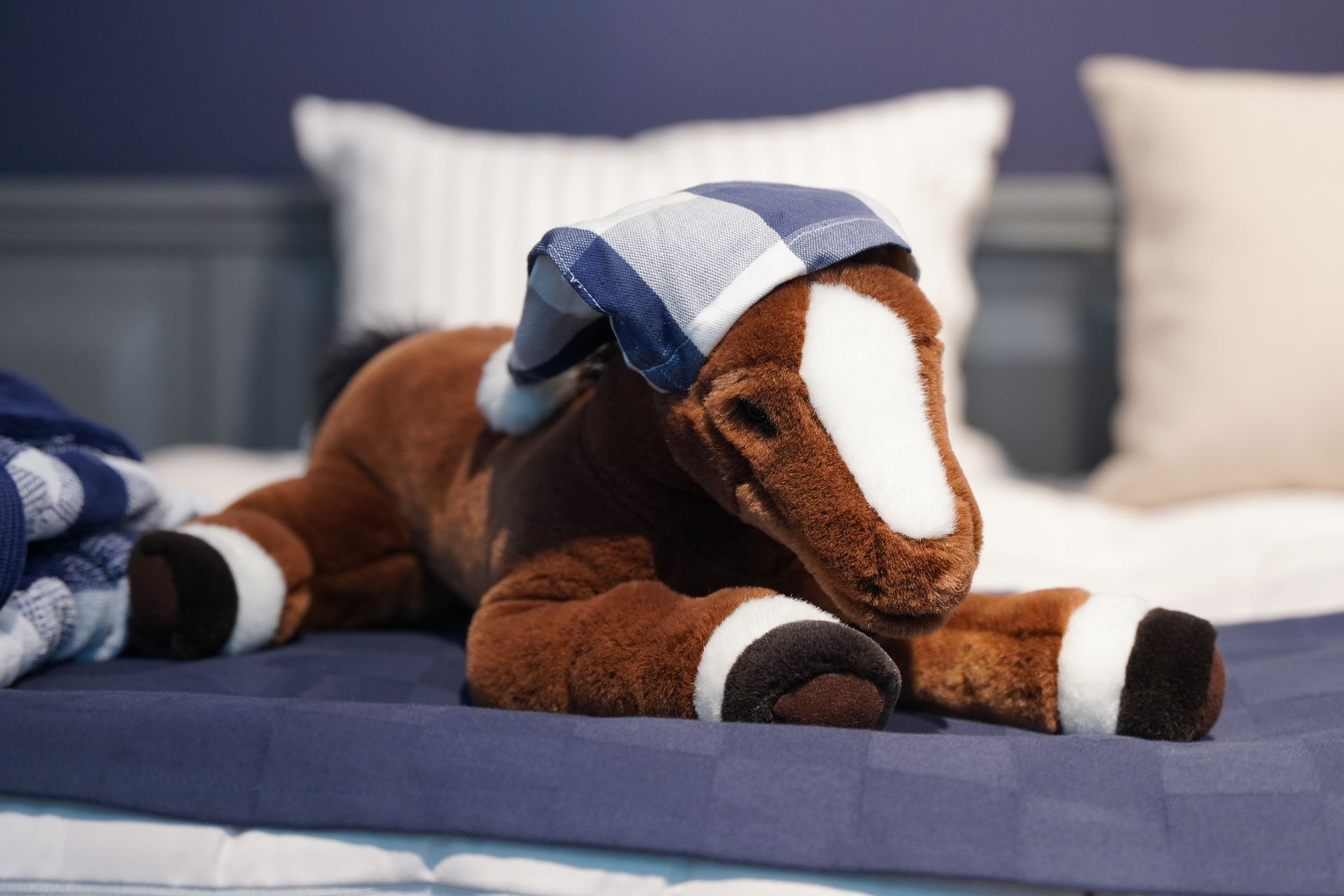 A stuffed horse is laying on a bed with a blanket on its head.