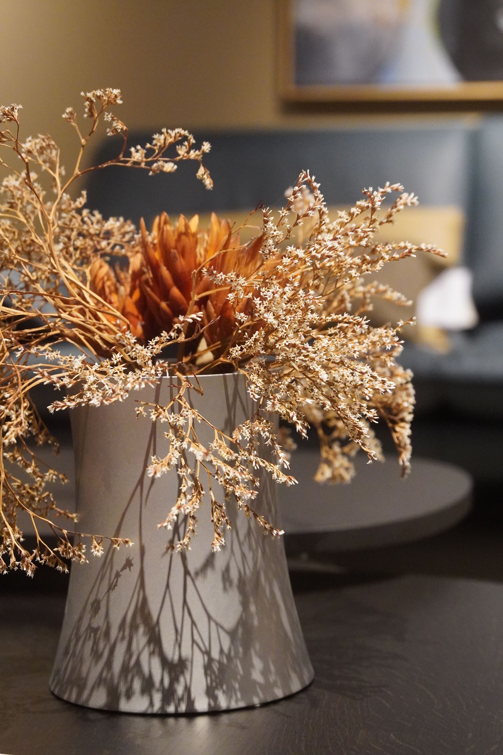 Op een tafel staat een vaas met gedroogde bloemen.