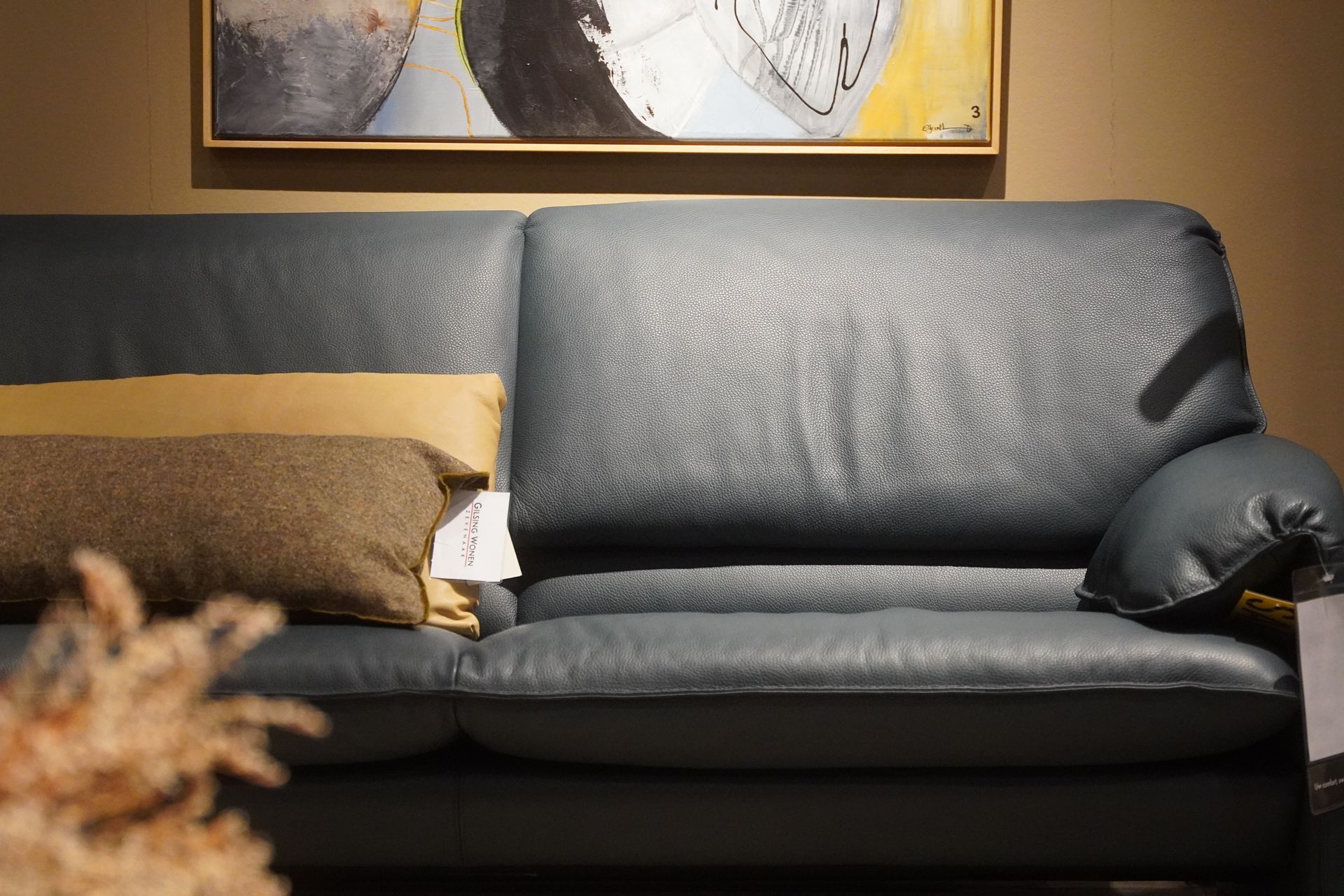 Gray leather sofa with two decorative pillows, under a painting.