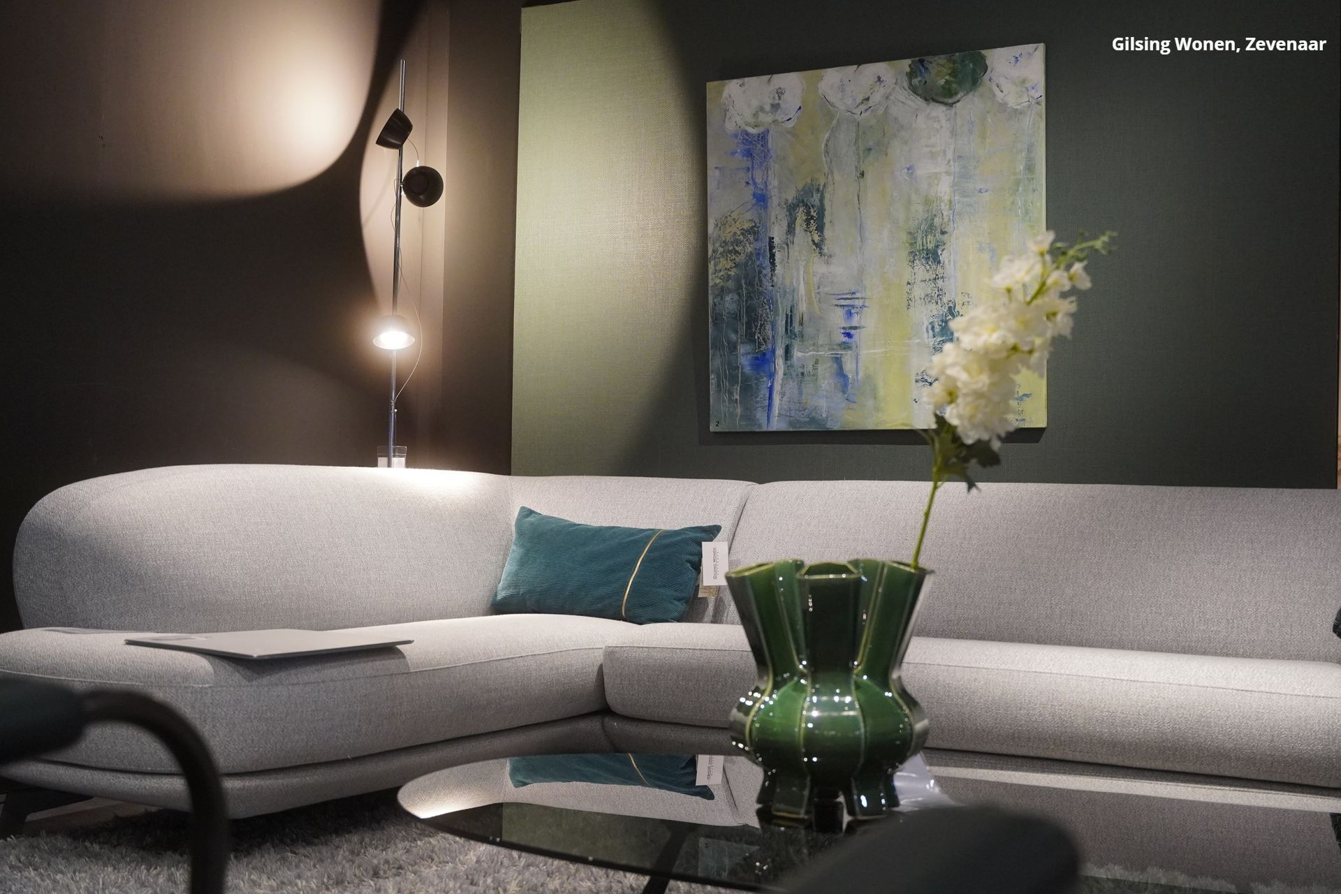 Een woonkamer met een hoekbank en een schilderij aan de muur