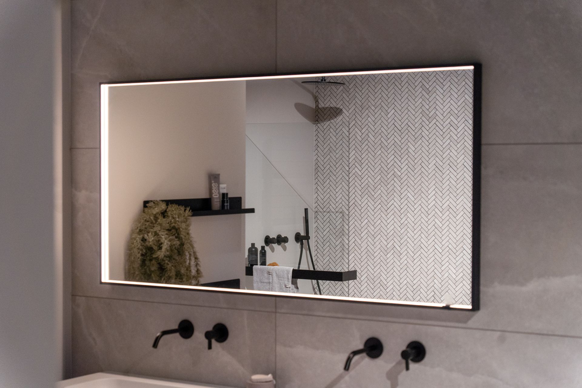 Rectangular bathroom mirror with LED lighting, black frame, above a sink with black faucets.