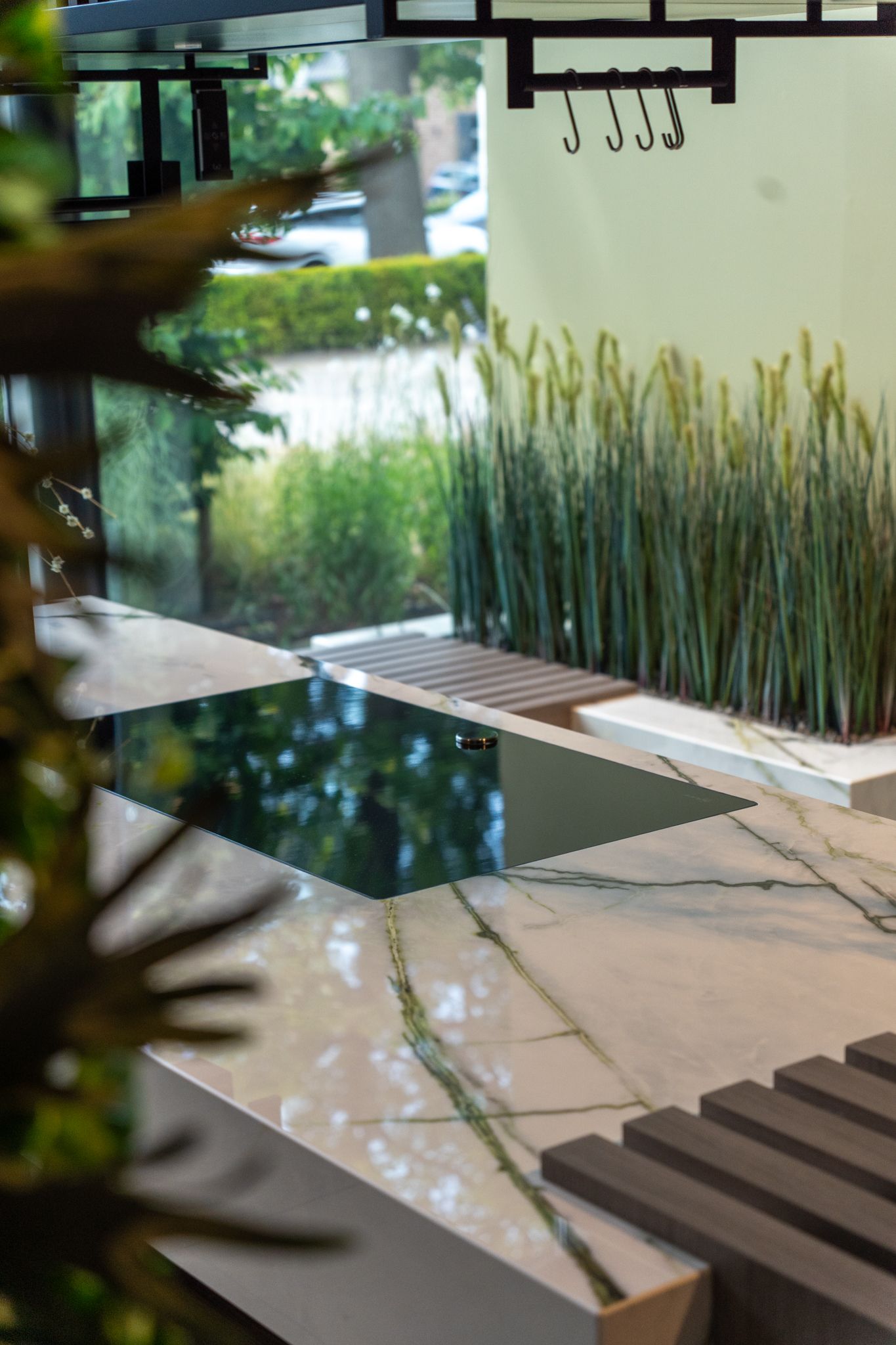 Modern kitchen counter with a dark cooktop, stone surface, and outdoor view with tall grass.