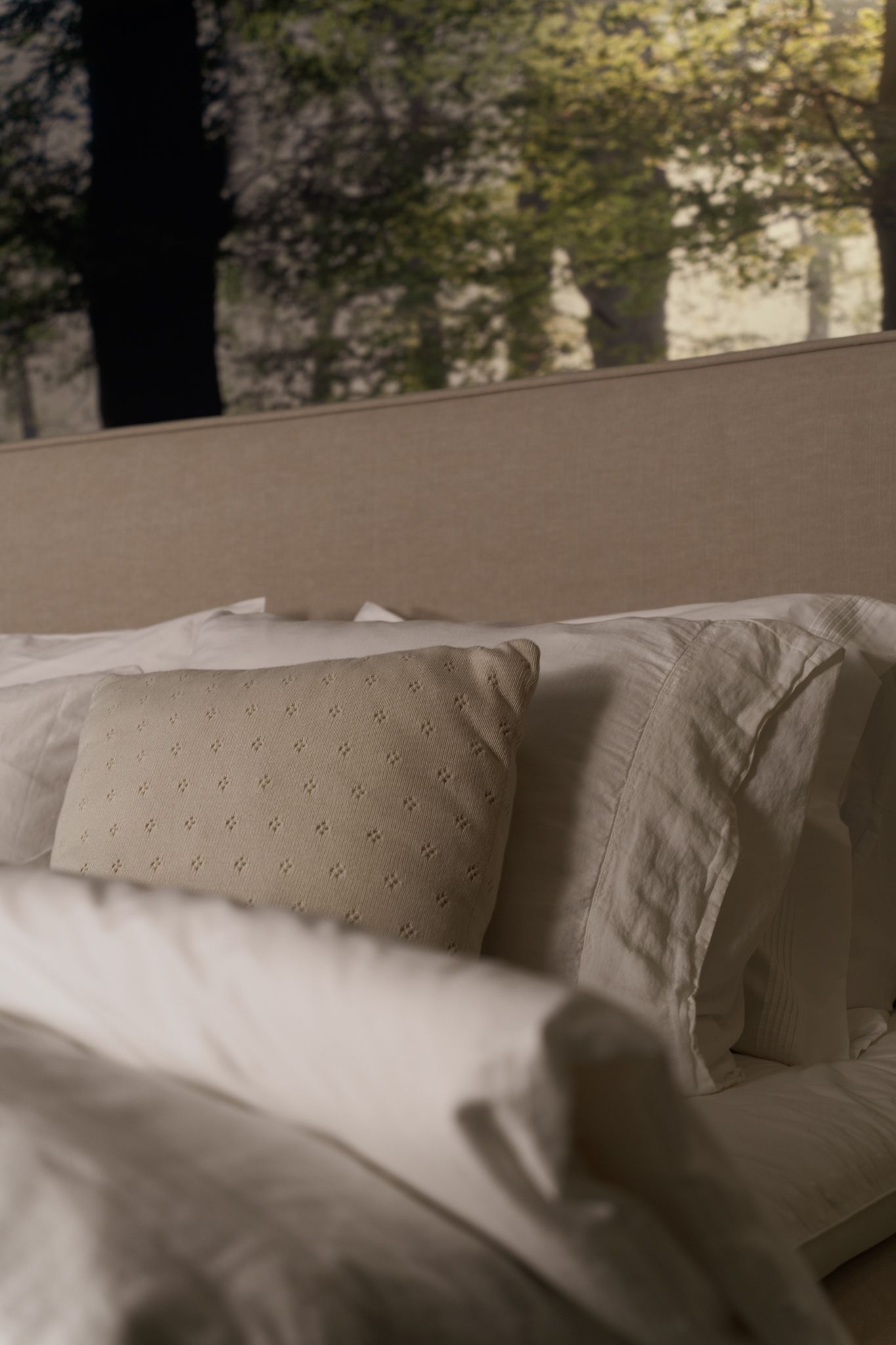 Bed with white linens and a textured beige pillow in front of a forest mural.