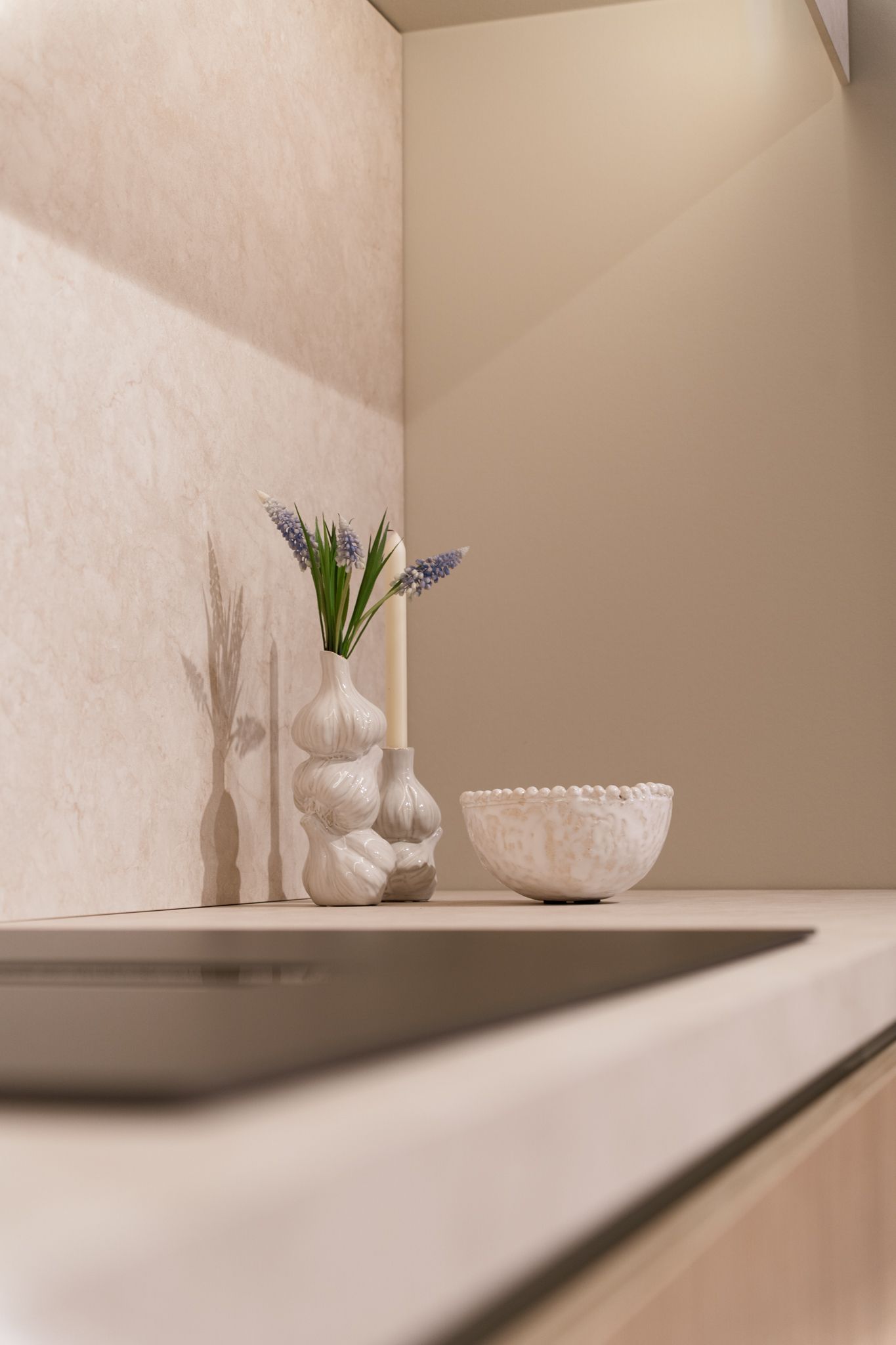 Corner kitchen countertop with white textured bowl, vase of flowers, and a thin candle.