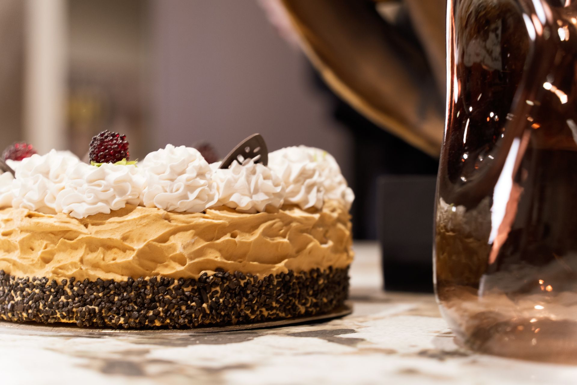 Cake with white frosting and berries on a marble surface. Next to a decorative glass object.