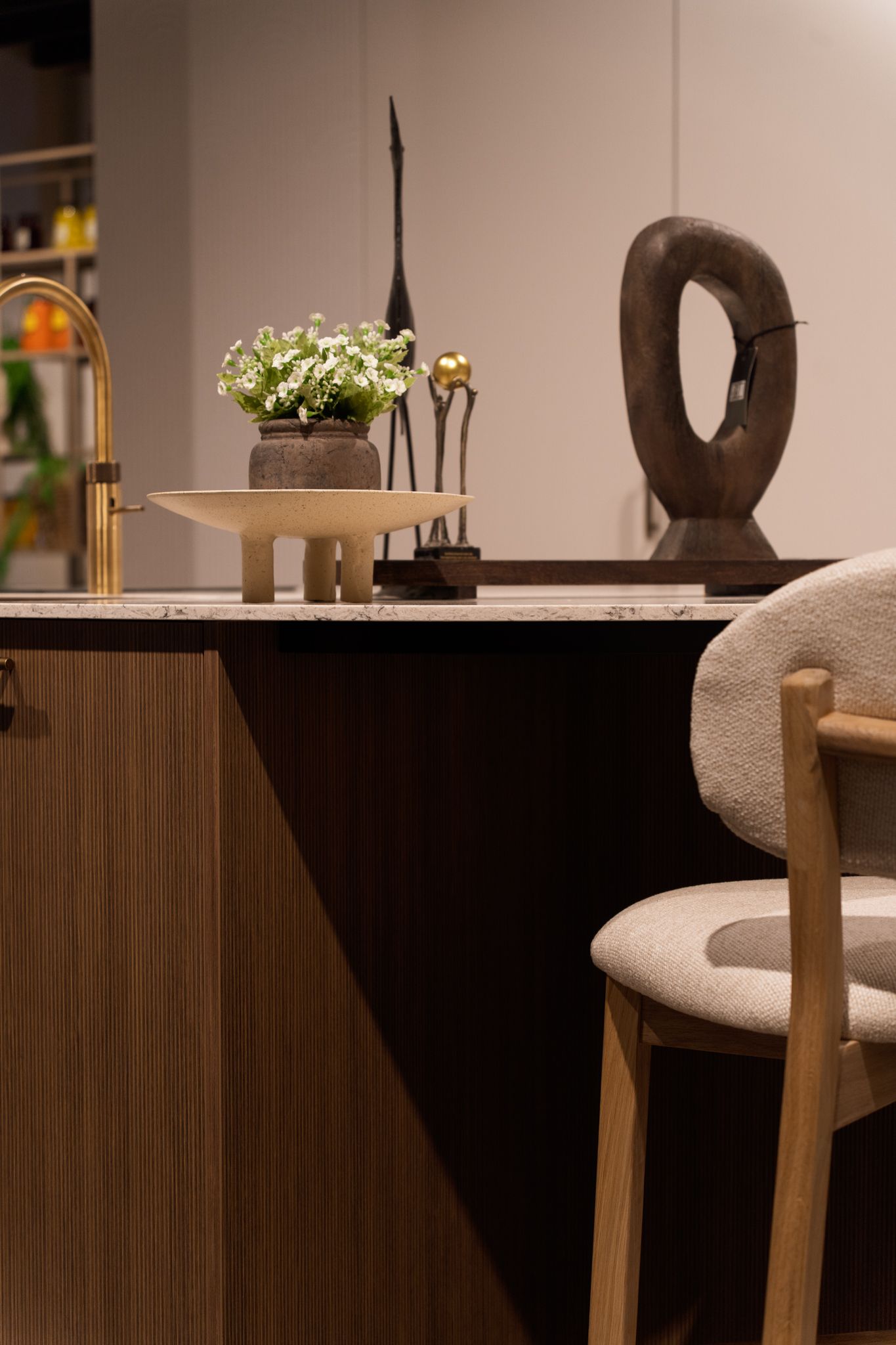 Close-up of a kitchen counter with decorative objects, including flowers, sculptures, and a chair.