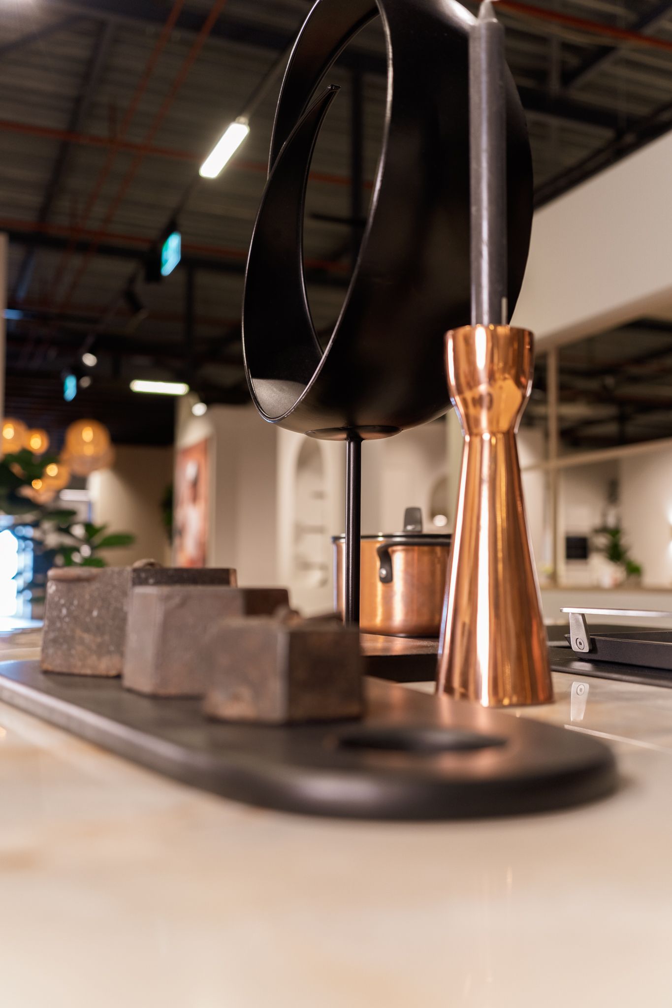 Copper and black home decor on a table. Includes a candle holder, sculptural element, and dark stone blocks.