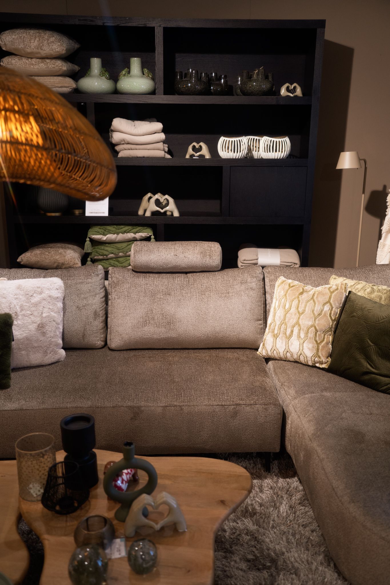 Woonkamer met bruine hoekbank, zwarte boekenkast en decoratieve objecten.