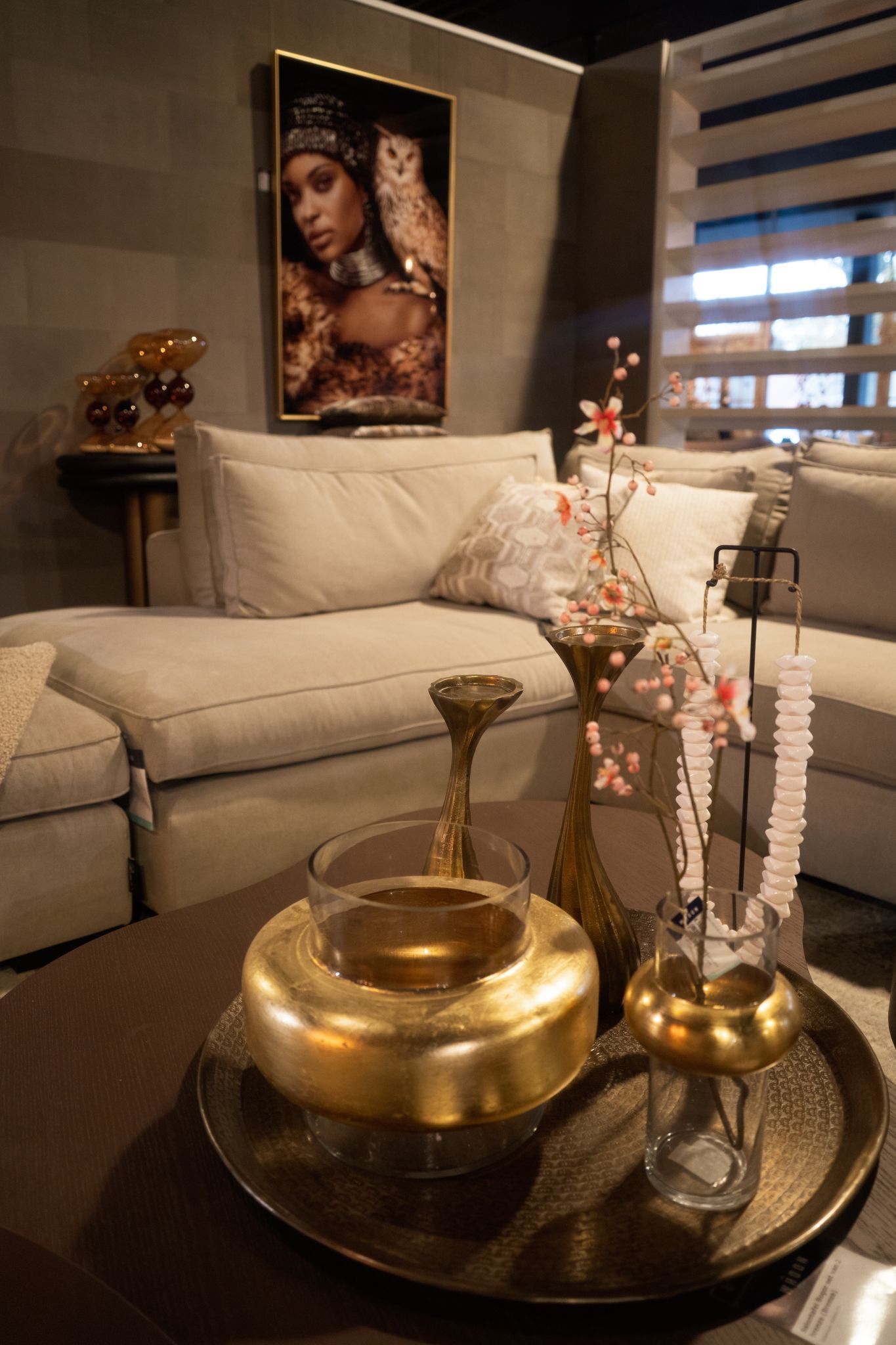 Elegante woonkamer met beige hoekbank, gouden decoratie en een bloemstuk op een donkere bijzettafel.