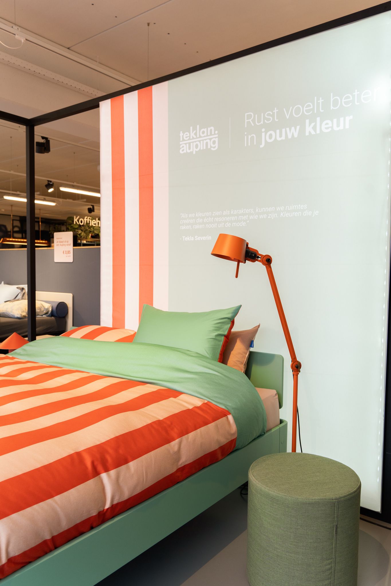 Bedroom display: Green bed with orange striped bedding, orange lamp, and green ottoman.