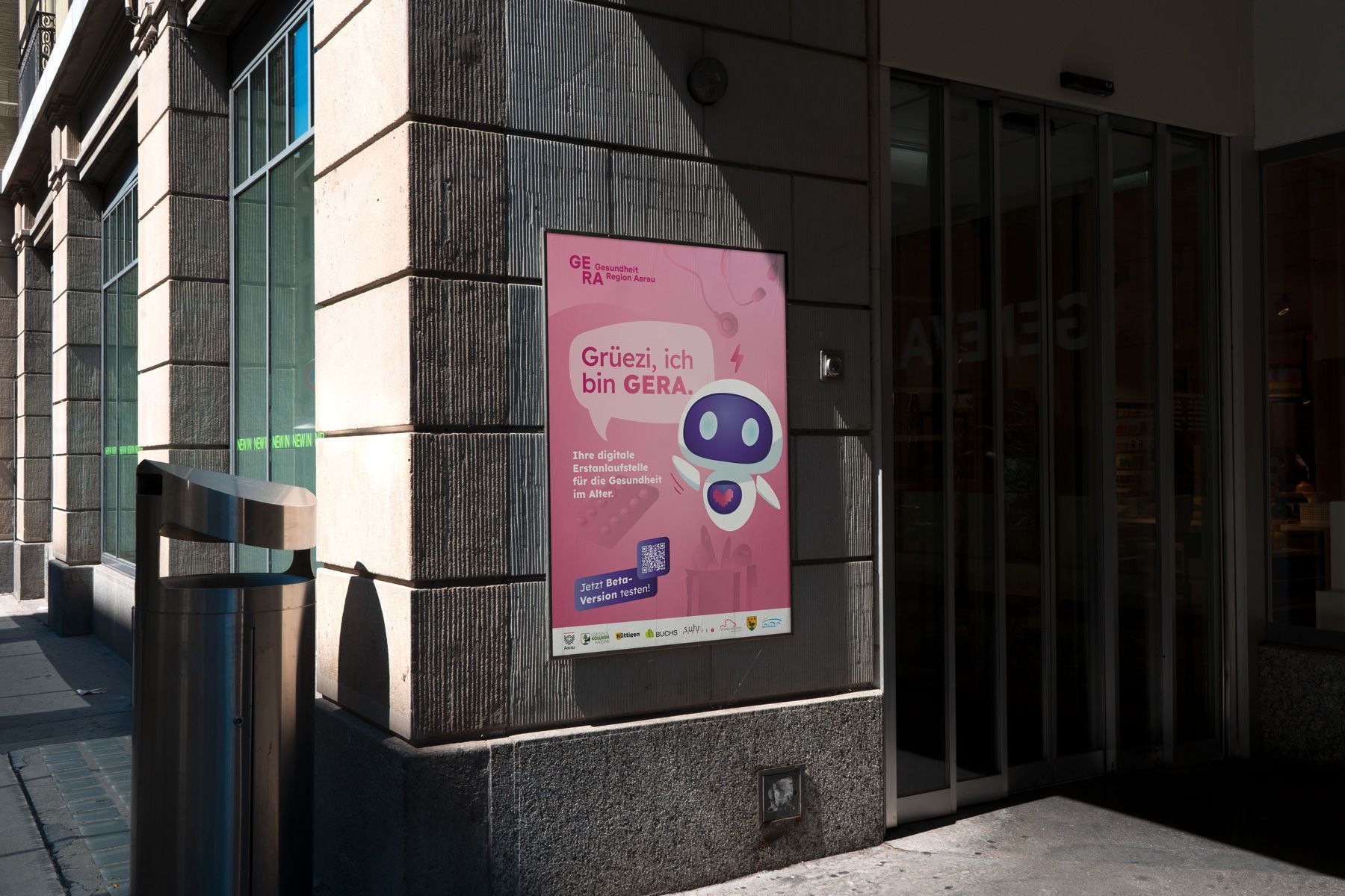 Ein pinkfarbenes Poster mit einem lila Comicgesicht hängt an einer Hauswand neben einem Glaseingang.