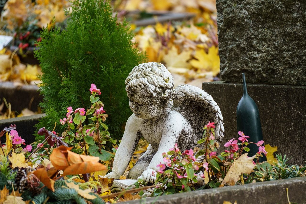 Picture of a tomb angel statue in a cemetery, with flowers and leaves around it
