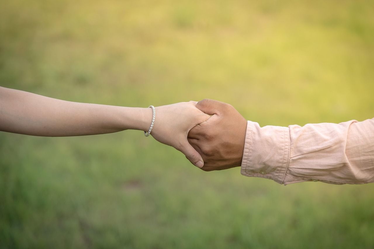2 people holding hands, with a grass background