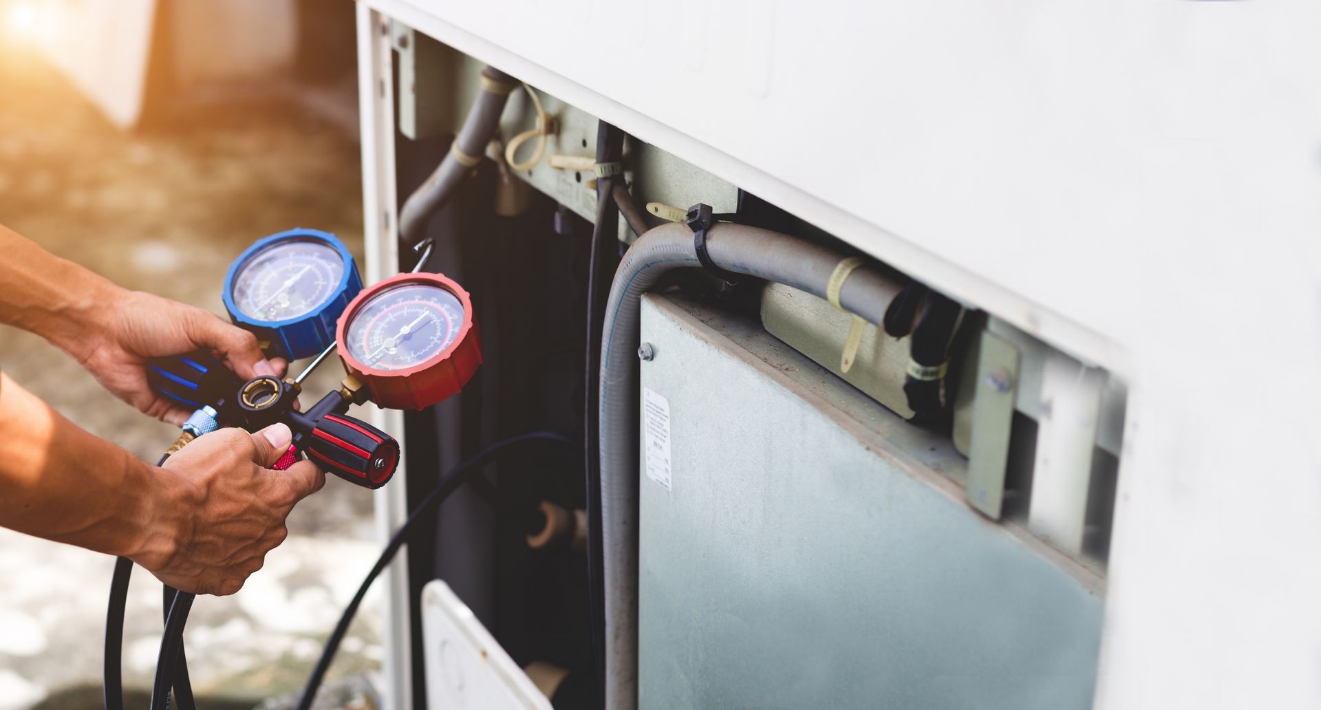 A man is working on an air conditioner with two gauges.
