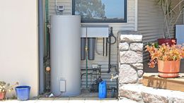A water heater is sitting outside of a house next to potted plants.