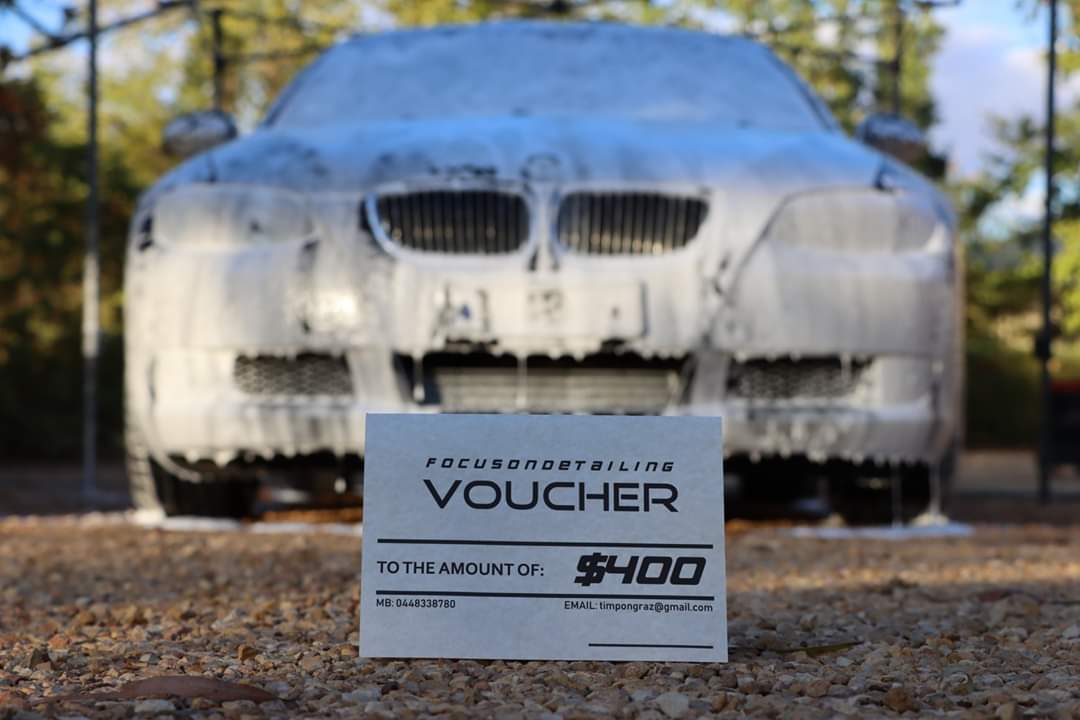 A voucher is sitting in front of a car covered in foam.