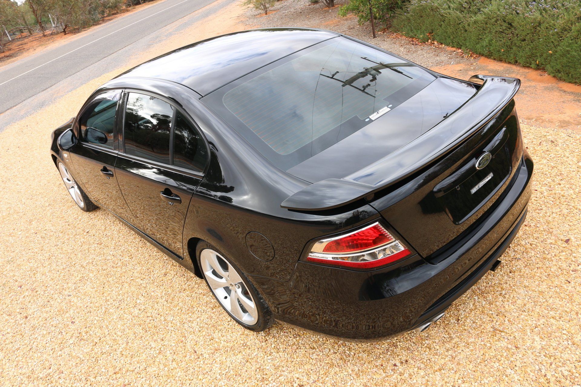 A black car is parked on gravel next to a road