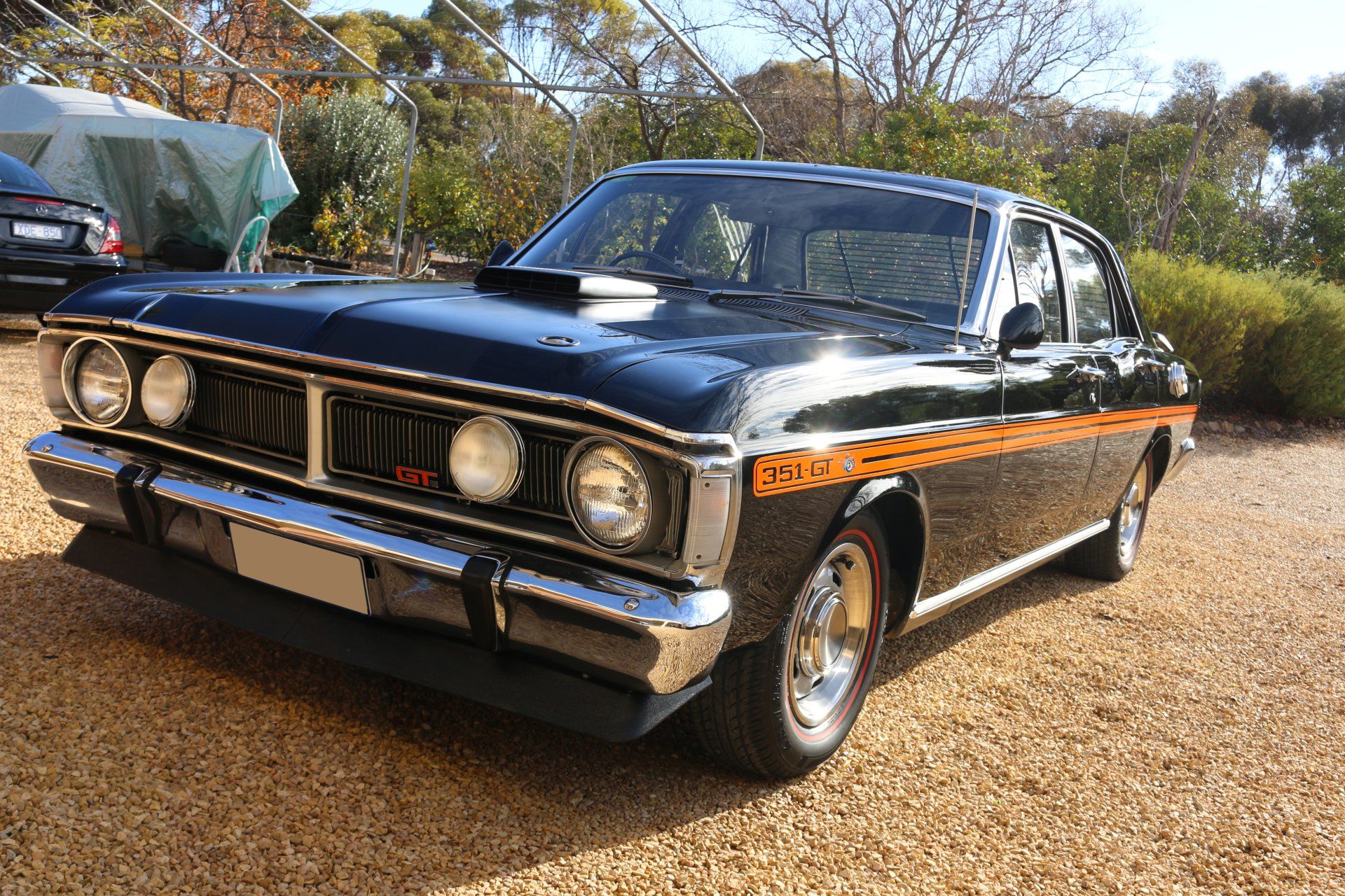 A black car with orange stripes on the side is parked on gravel.