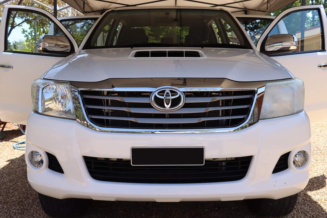 The front of a white toyota hilux with its doors open.