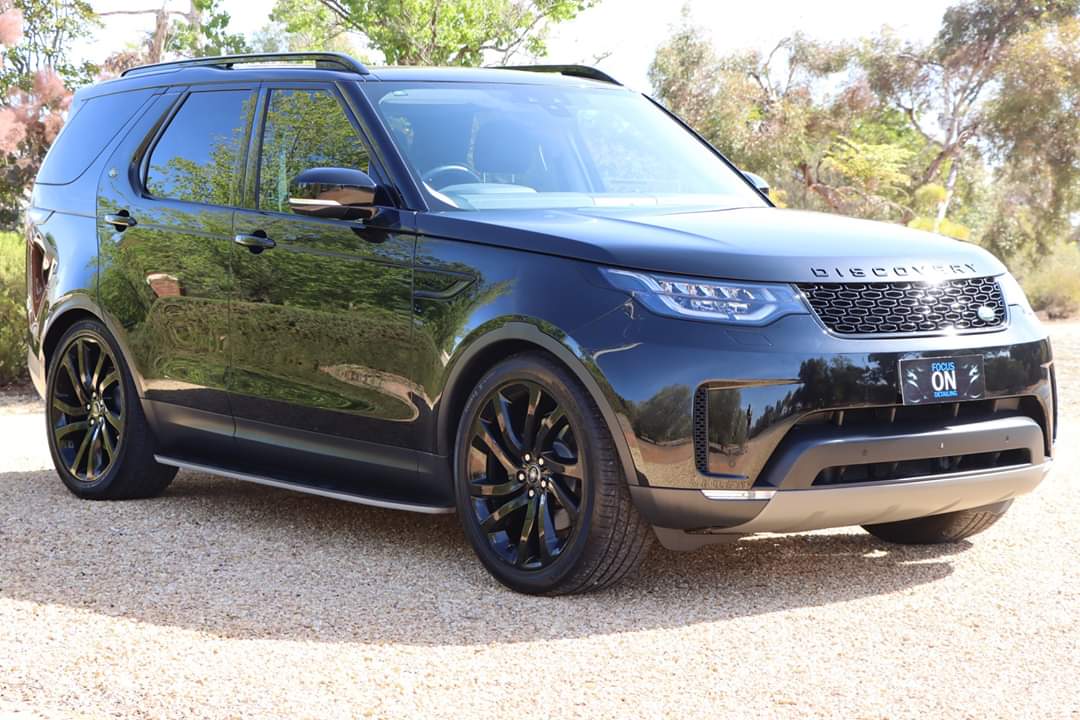 A black range rover discovery is parked in a gravel lot.