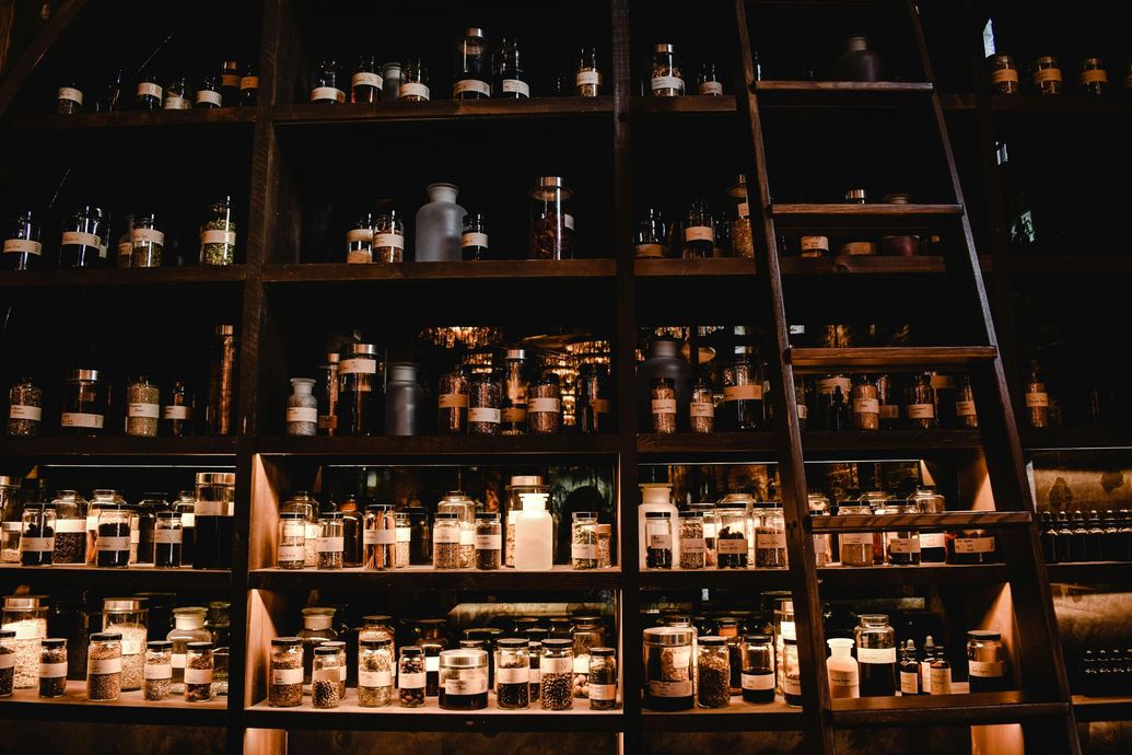 Wooden shelves filled with glass jars and bottles, lit from within. A ladder leans against the shelves.