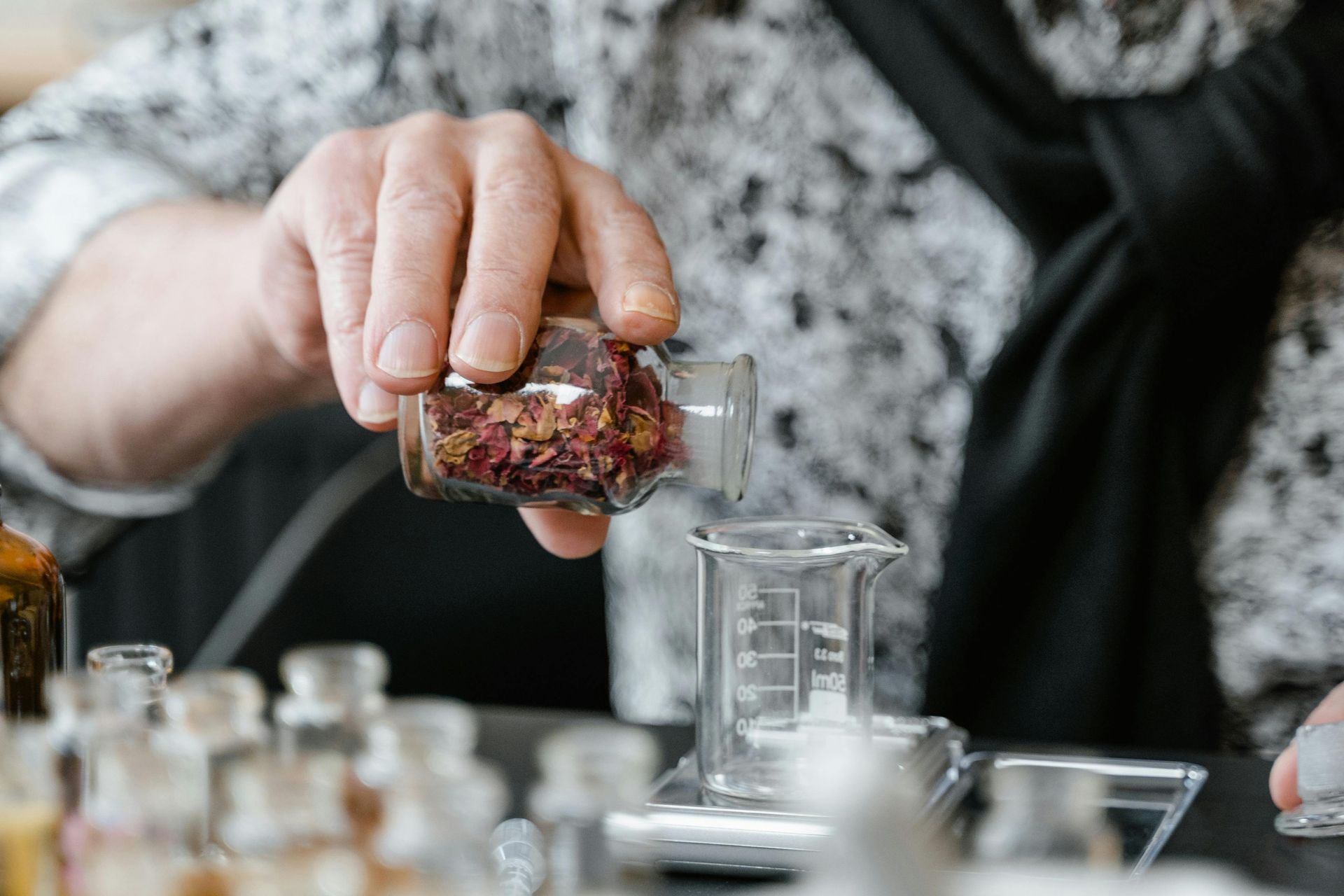Person pouring dried petals from a small jar into a beaker; other vials are on a lab counter.