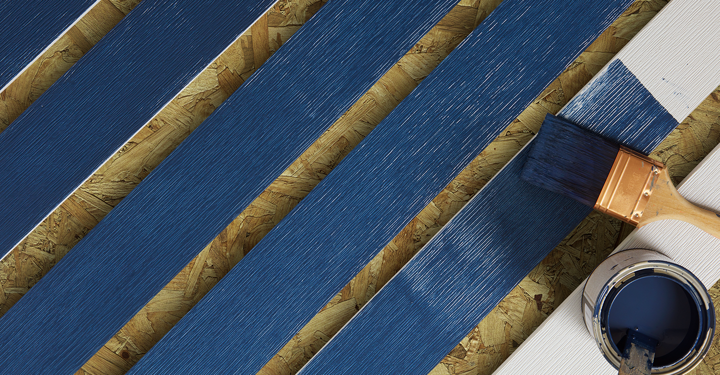 A brush and a can of blue paint are sitting on a wooden surface.