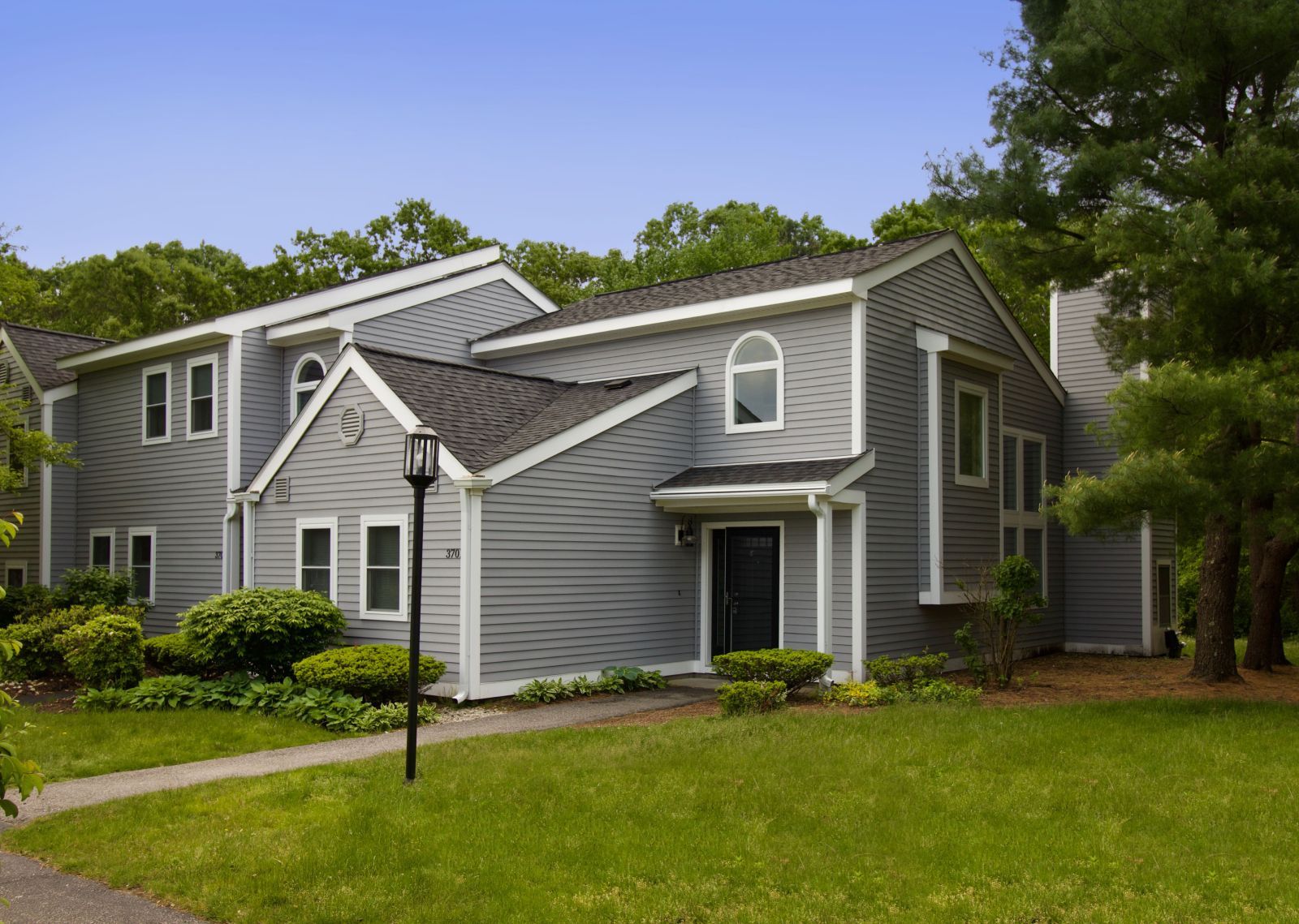 A gray house with a black door is surrounded by trees and grass